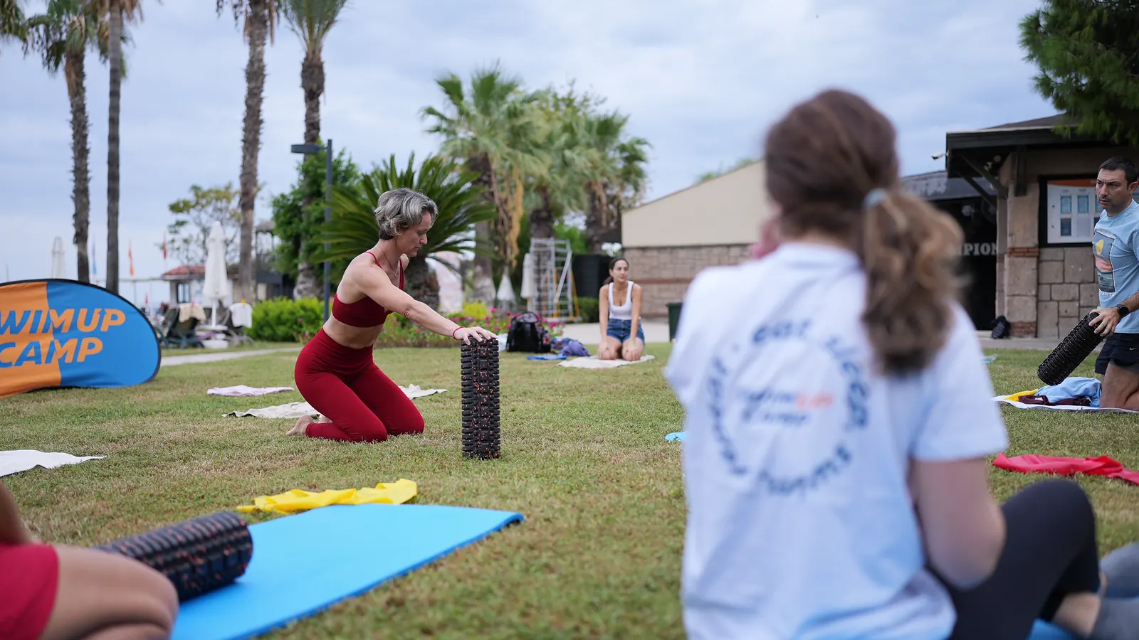 October 2026, Kemer, early morning: participants stretch and loosen up on mats on the lawn.