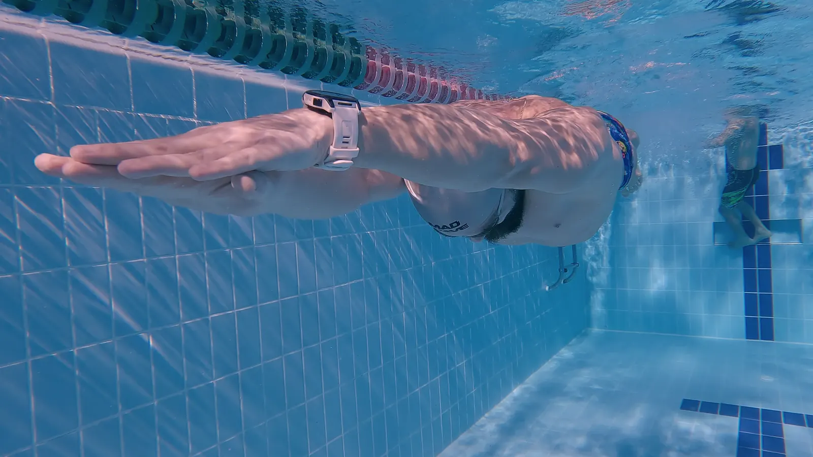 Underwater camera: an extended arm and the hand's entry, close up beneath the lane rope.
