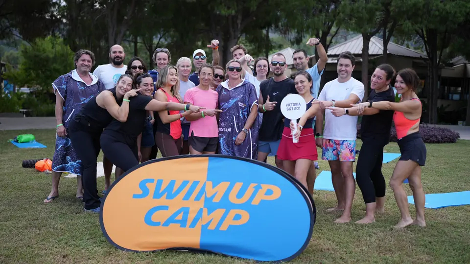Swim Up Camp tabelasının arkasında kalabalık grup, hep birlikte kameraya işaret ediyor.