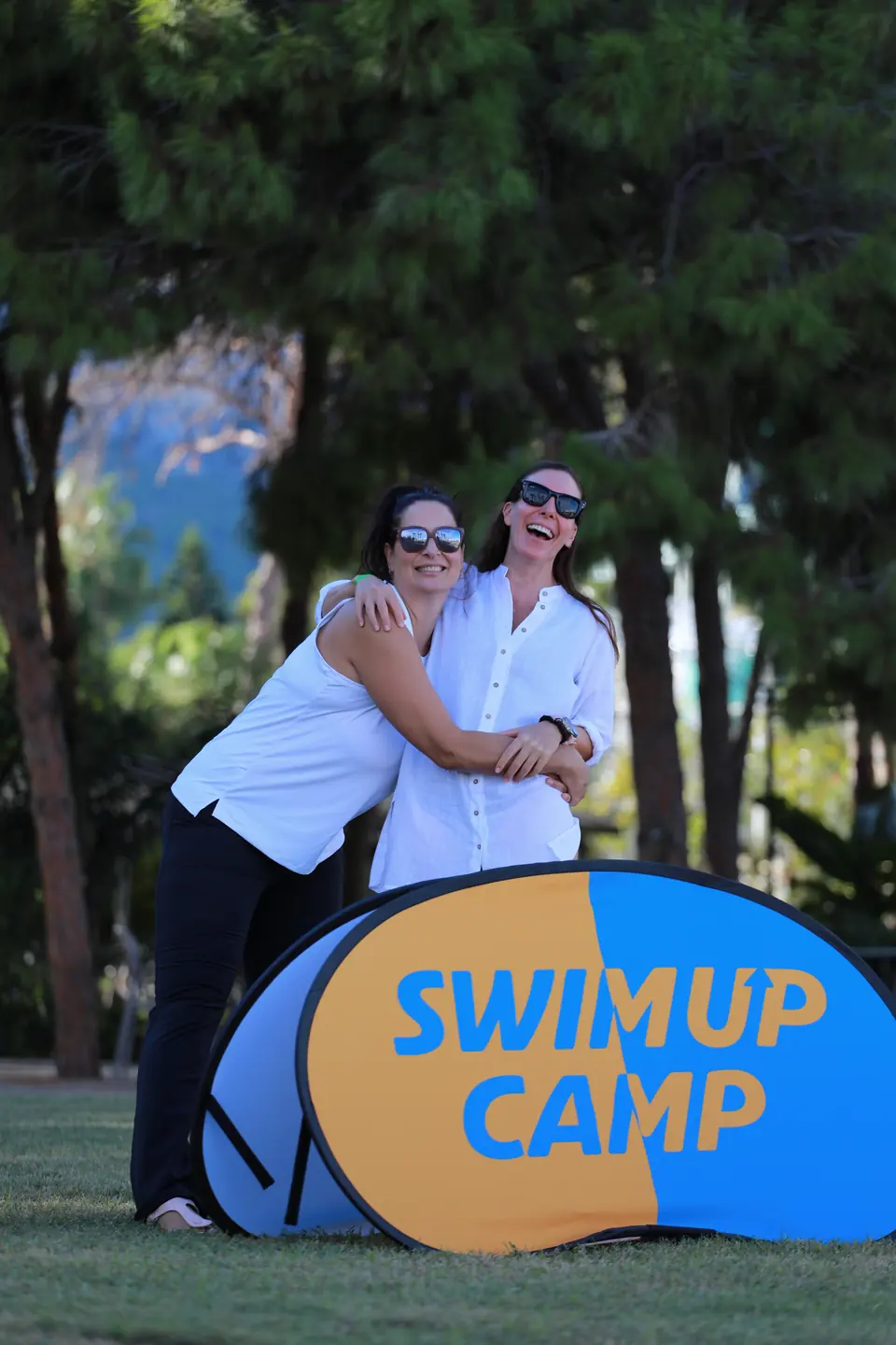 İki katılımcı Swim Up Camp tabelasının yanında sarılıyor.