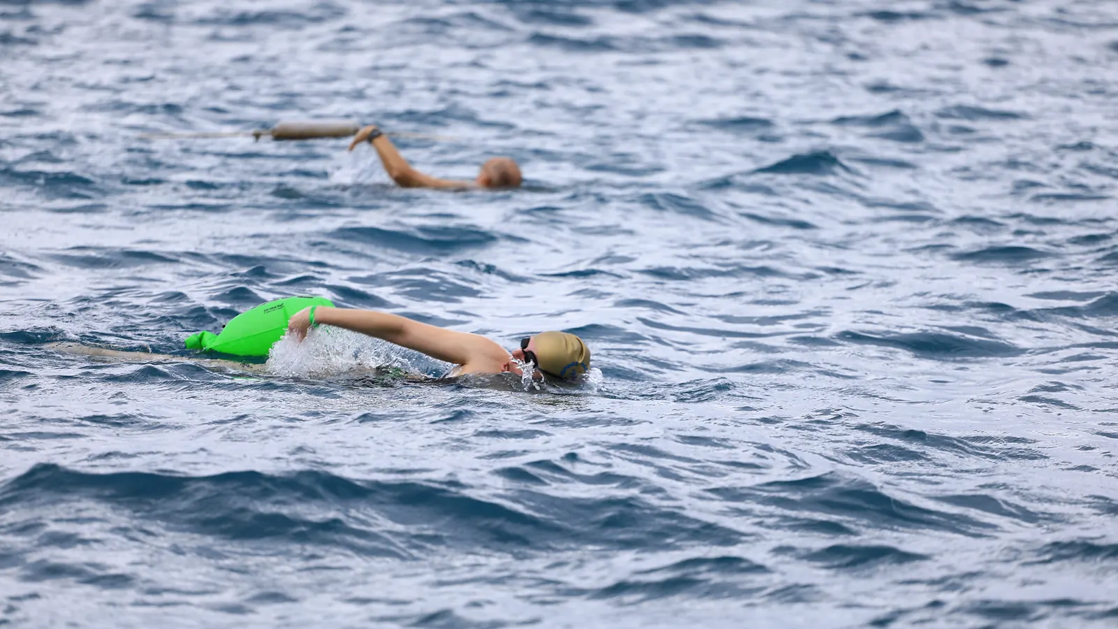 Ekim 2026, Kemer: açık denizde yeşil tow float'ıyla sağa ilerleyen bir yüzücü, uzakta ikinci bir katılımcı.