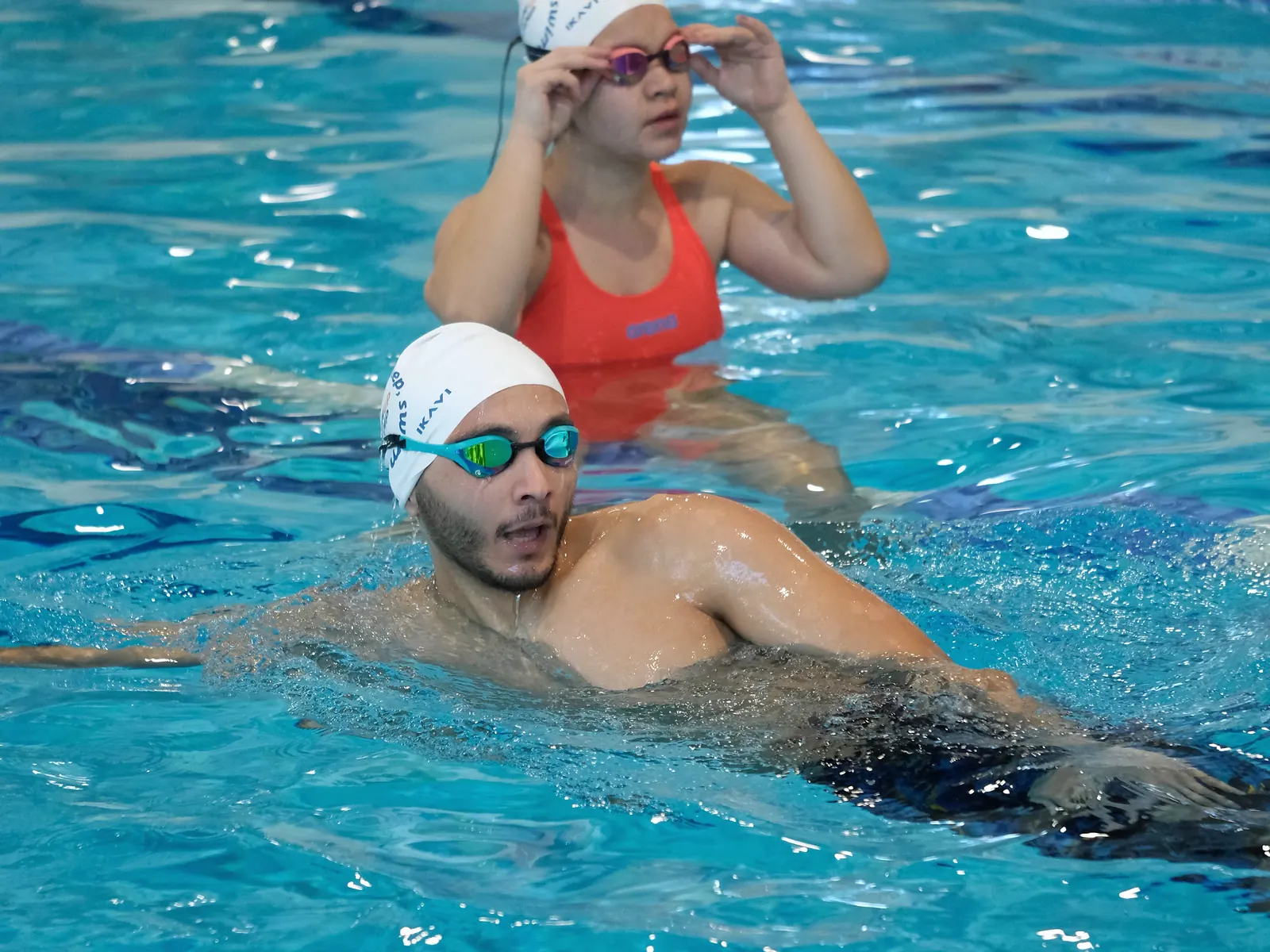 Şubat 2025, Gloria Sports Arena kapalı havuzu: kulvarda dinlenen iki katılımcı, Swim Up boneleriyle.